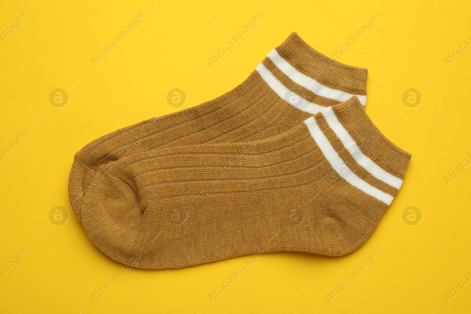 Photo of Pair of soft socks on yellow background, top view