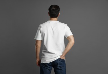 Photo of Man in blank white t-shirt on grey background, back view. Mockup for design