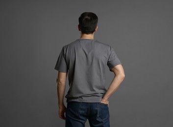 Photo of Man in blank t-shirt on grey background, back view. Mockup for design