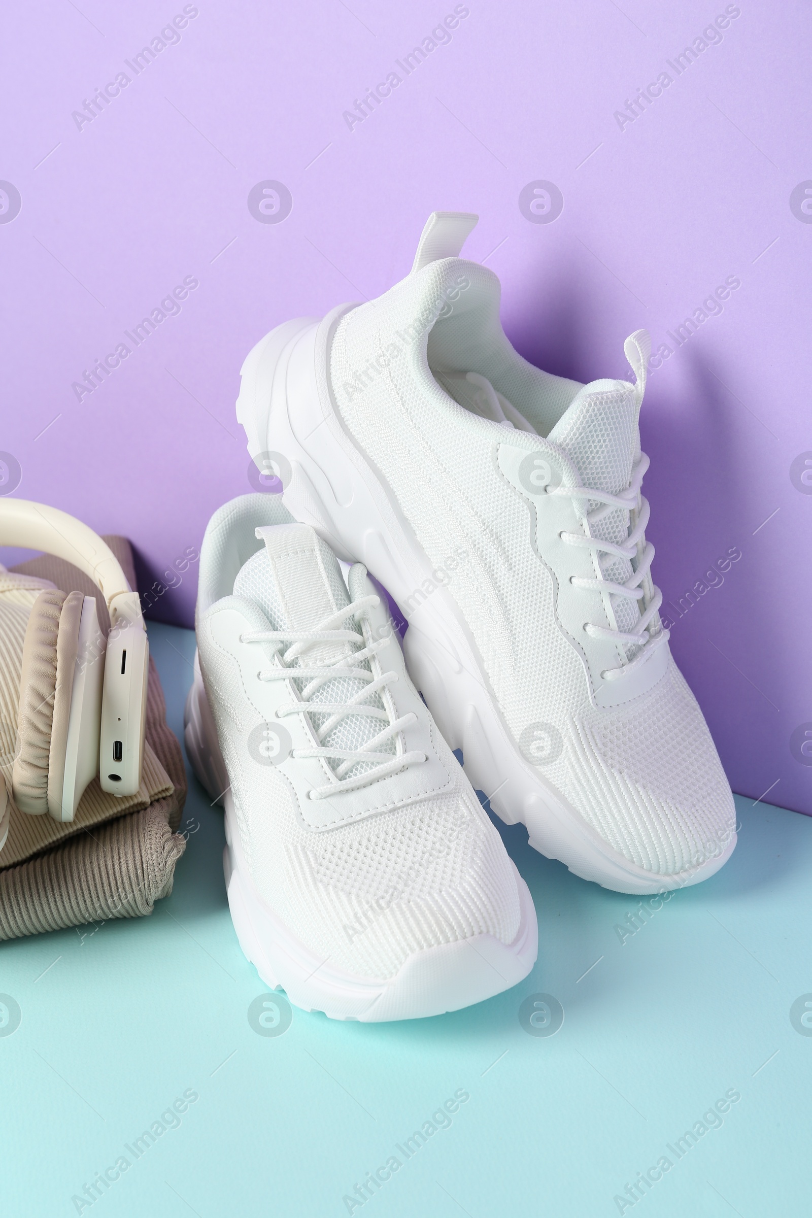 Photo of Pair of stylish white sneakers, sportswear and headphones on color background