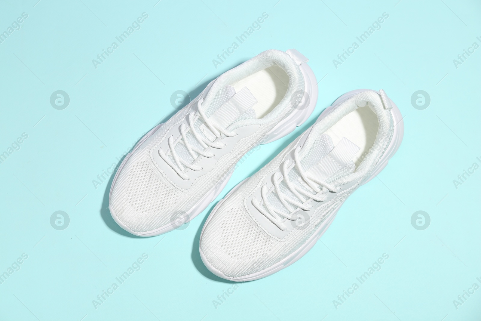 Photo of Pair of stylish white sneakers on light blue background, top view