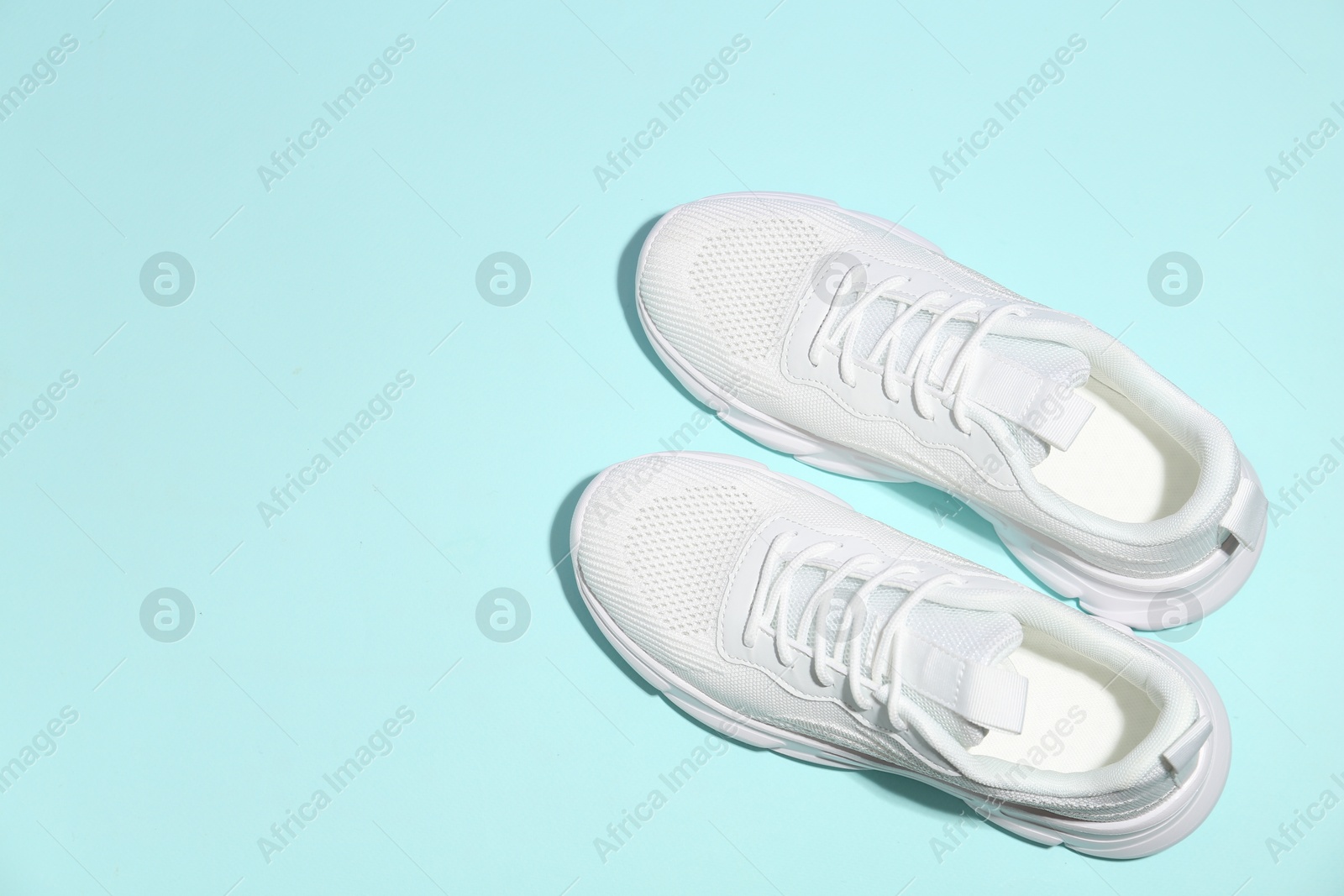 Photo of Pair of stylish white sneakers on light blue background, top view. Space for text