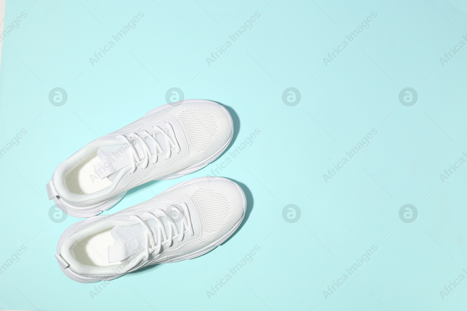 Photo of Pair of stylish white sneakers on light blue background, top view. Space for text