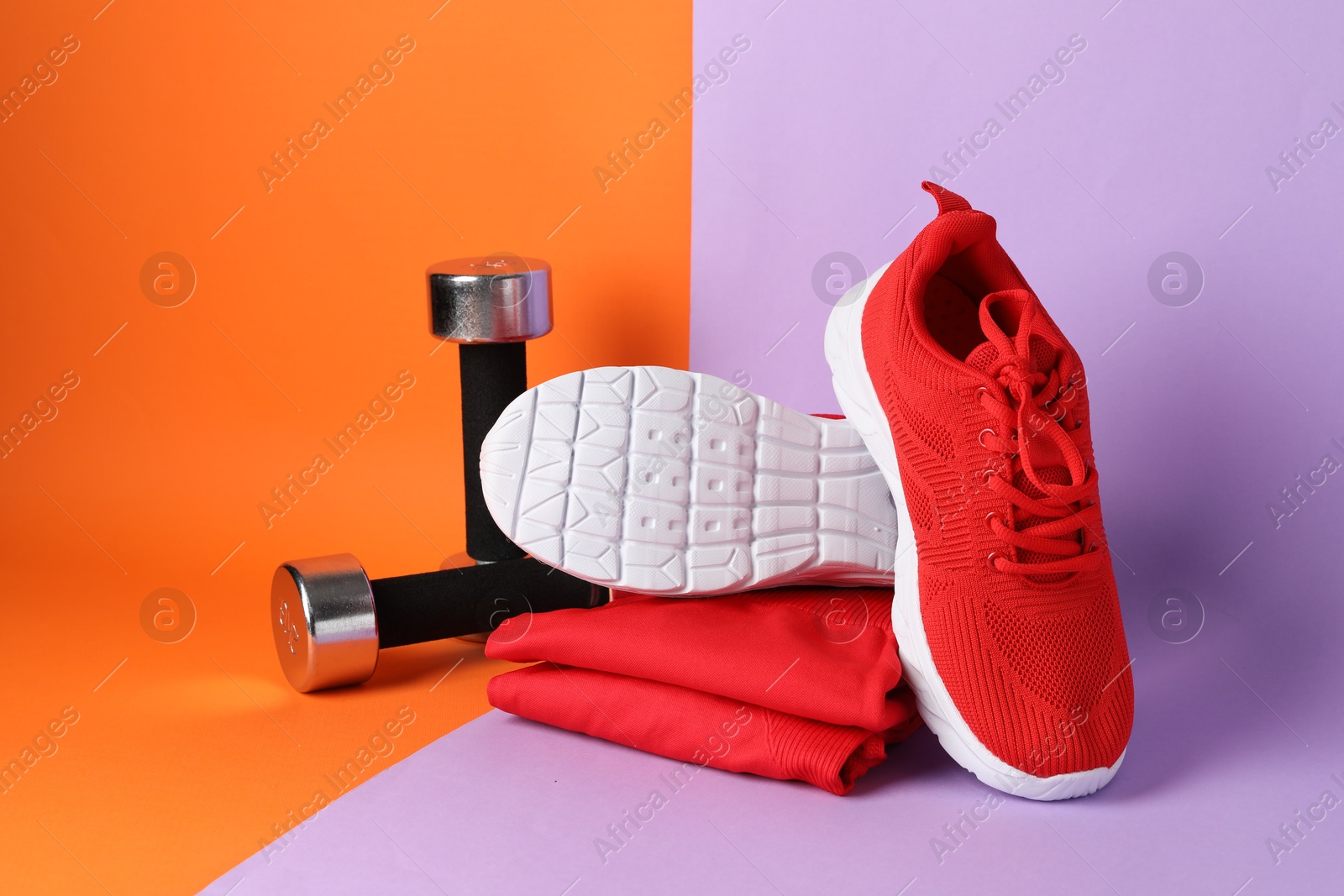 Photo of Pair of stylish red sneakers, sportswear and dumbbells on color background