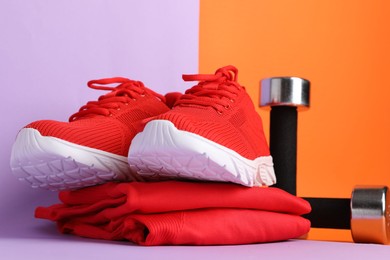 Photo of Pair of stylish red sneakers, sportswear and dumbbells on color background, closeup