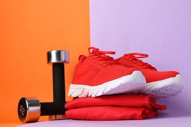 Photo of Pair of stylish red sneakers, sportswear and dumbbells on color background