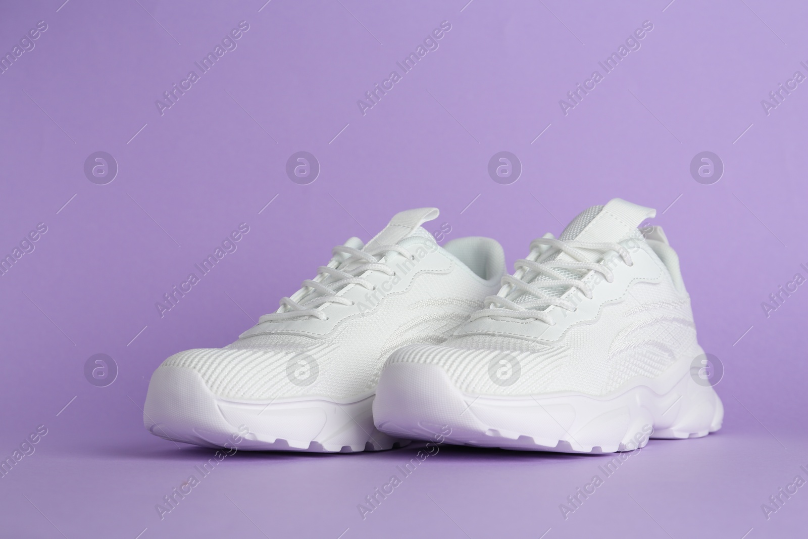 Photo of Pair of stylish white sneakers on violet background