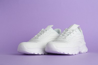 Photo of Pair of stylish white sneakers on violet background