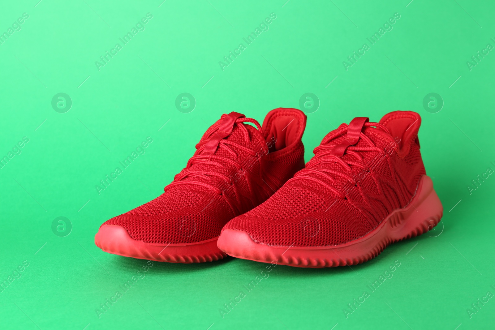 Photo of Pair of stylish red sneakers on green background