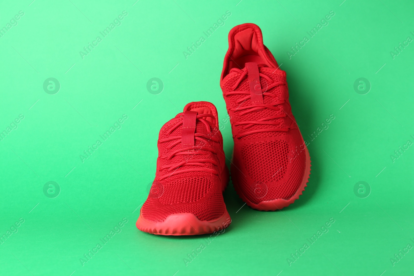 Photo of Pair of stylish red sneakers on green background