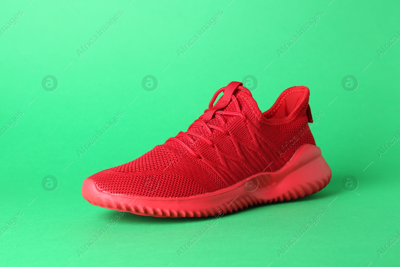 Photo of Stylish red sneaker on green background. Sports footwear