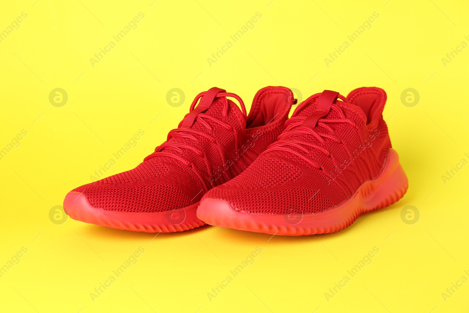 Photo of Pair of stylish red sneakers on yellow background