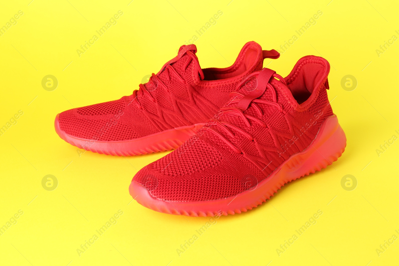 Photo of Pair of stylish red sneakers on yellow background