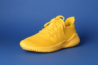 Photo of Stylish yellow sneaker on blue background. Sports footwear