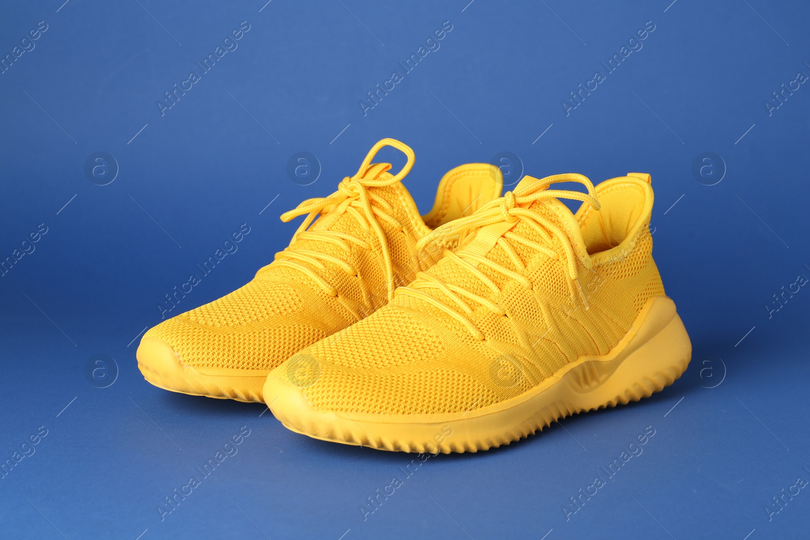 Photo of Pair of stylish yellow sneakers on blue background