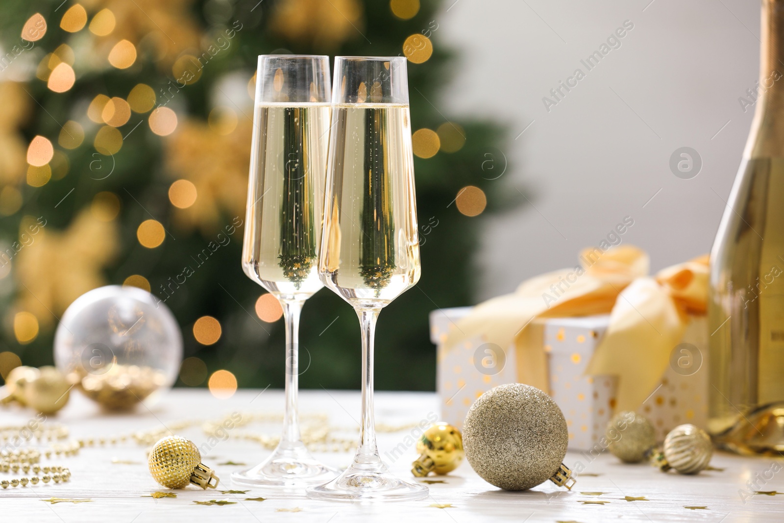 Photo of Champagne in glasses and Christmas decor on white wooden table against blurred lights. Bokeh effect