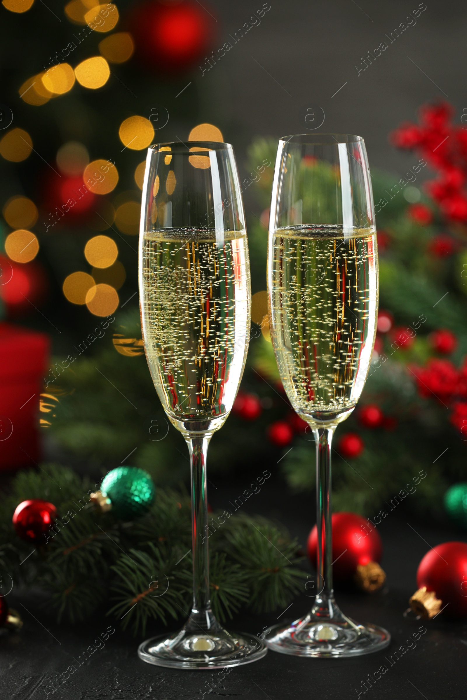 Photo of Champagne in glasses and decor on black table against blurred Christmas lights