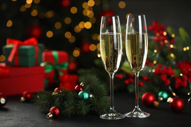 Photo of Champagne in glasses and decor on black table against blurred Christmas lights, space for text