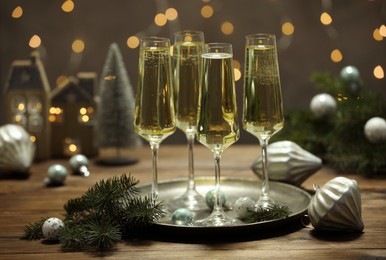 Photo of Champagne in glasses and Christmas decor on wooden table against blurred lights. Bokeh effect