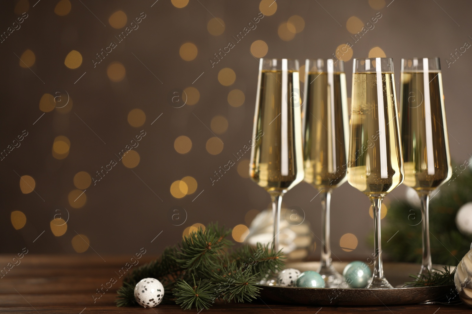 Photo of Champagne in glasses and decor on wooden table against blurred Christmas lights, space for text. Bokeh effect