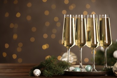 Photo of Champagne in glasses and decor on wooden table against blurred Christmas lights, space for text. Bokeh effect