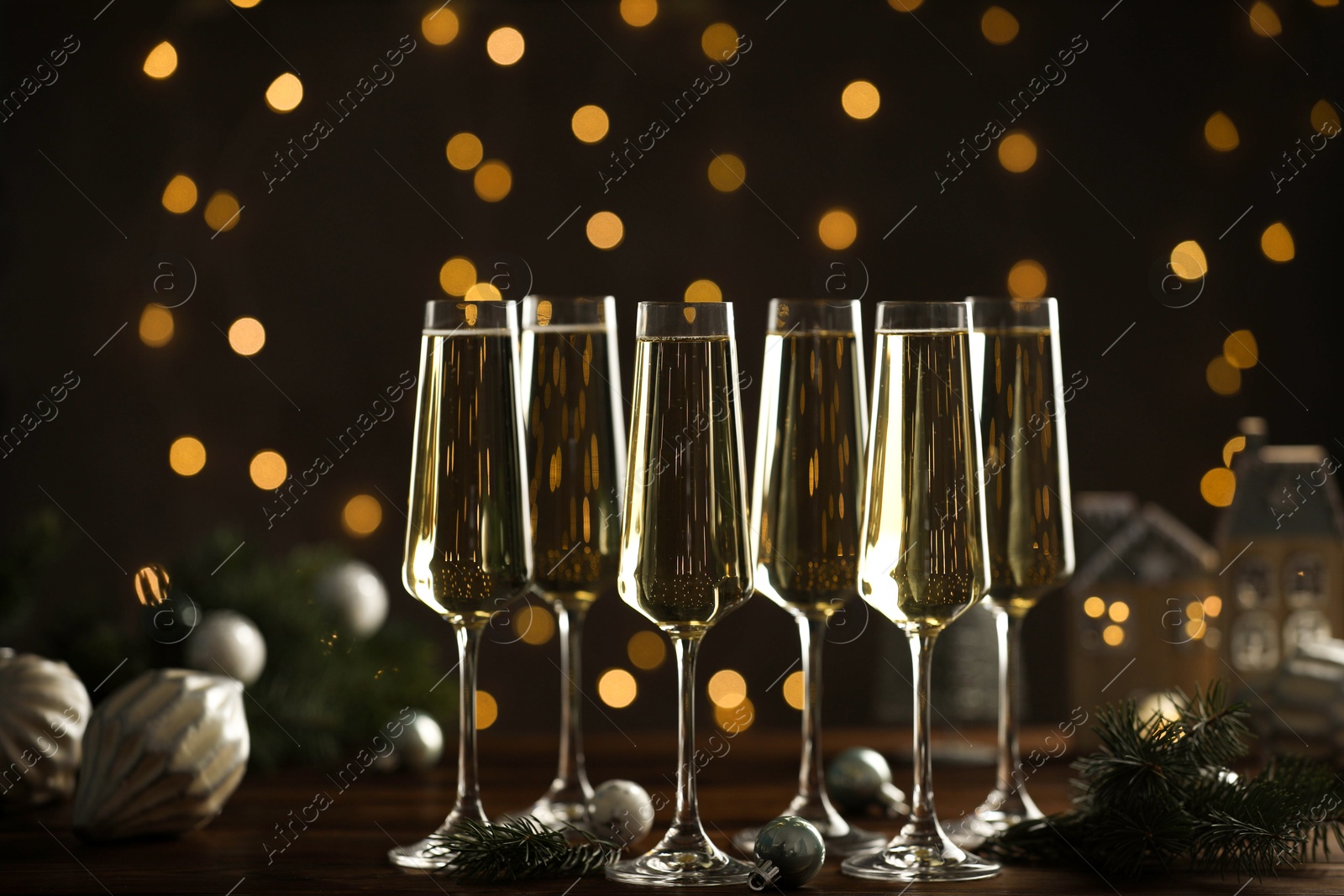 Photo of Champagne in glasses and Christmas decor on wooden table against blurred lights. Bokeh effect