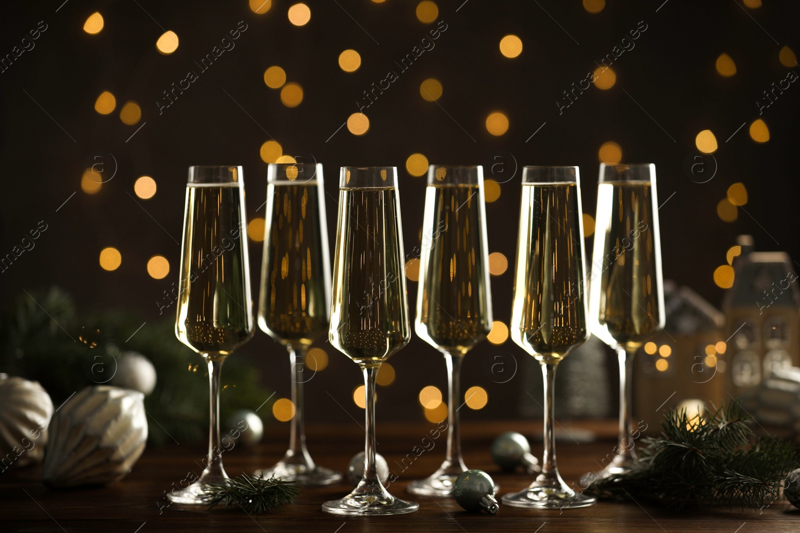 Photo of Champagne in glasses and Christmas decor on wooden table against blurred lights. Bokeh effect