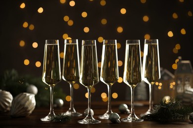 Photo of Champagne in glasses and Christmas decor on wooden table against blurred lights. Bokeh effect