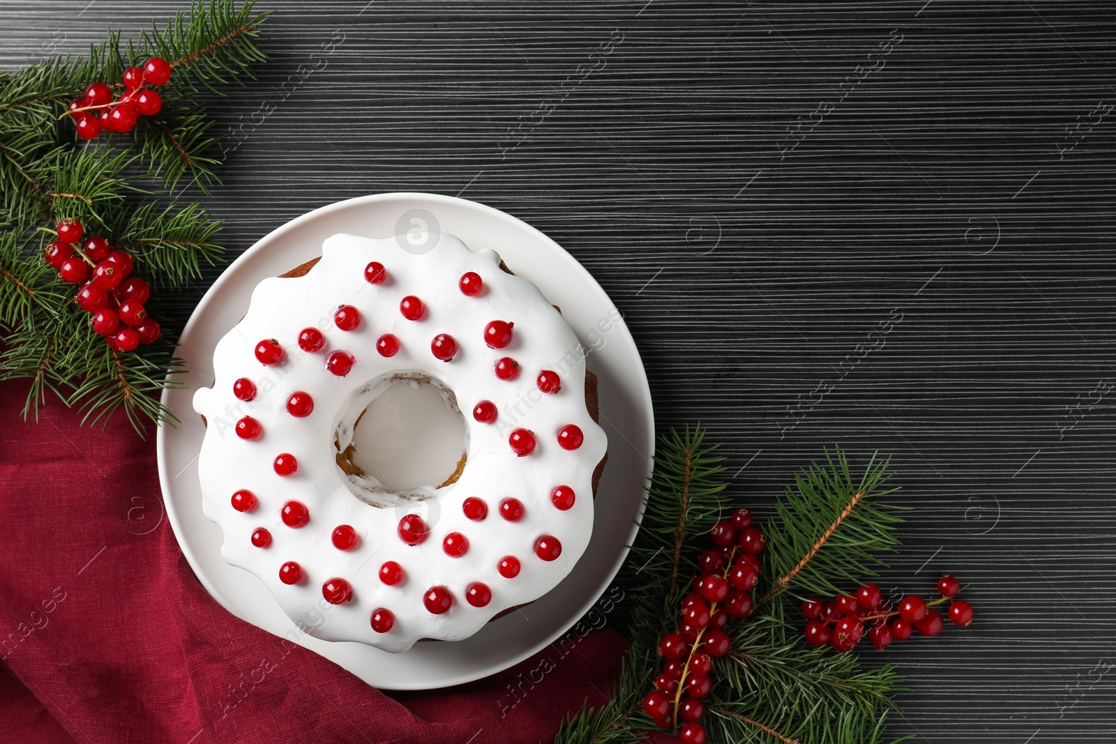 Photo of Tasty Christmas cake with red currants and fir branches on black wooden table, flat lay. Space for text