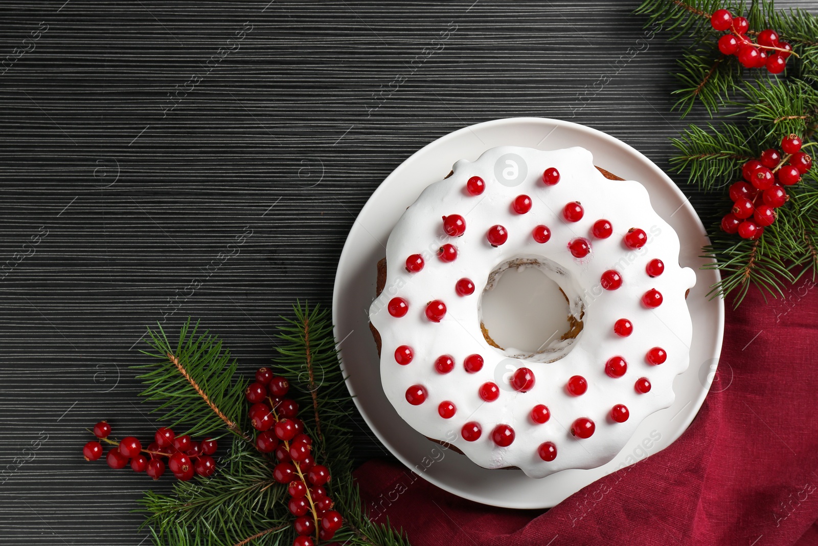 Photo of Tasty Christmas cake with red currants and fir branches on black wooden table, flat lay. Space for text