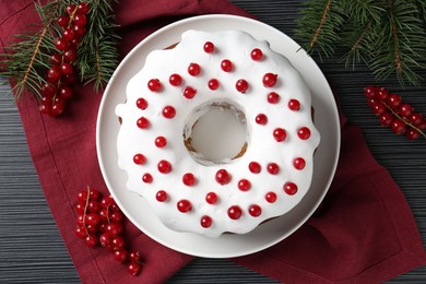 Photo of Tasty Christmas cake with red currants and fir branches on black wooden table, flat lay