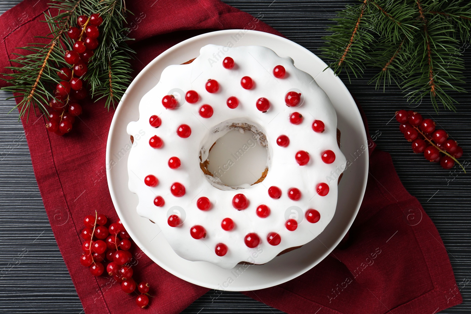 Photo of Tasty Christmas cake with red currants and fir branches on black wooden table, flat lay