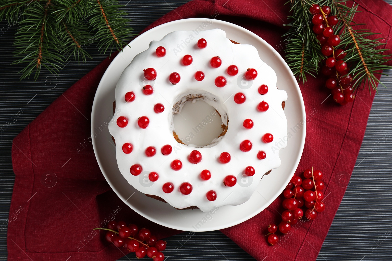 Photo of Tasty Christmas cake with red currants and fir branches on black wooden table, flat lay