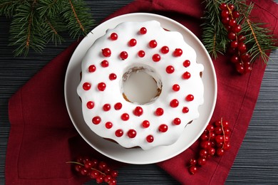 Photo of Tasty Christmas cake with red currants and fir branches on black wooden table, flat lay