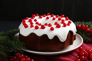 Photo of Tasty Christmas cake with red currants and fir branches on table against dark background, closeup