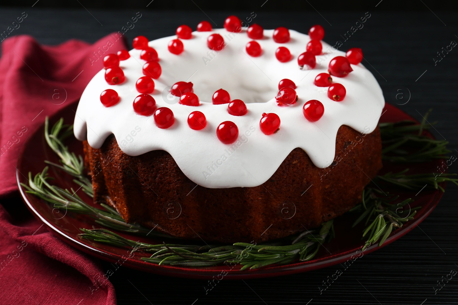 Photo of Tasty Christmas cake with red currants and rosemary on black table, closeup