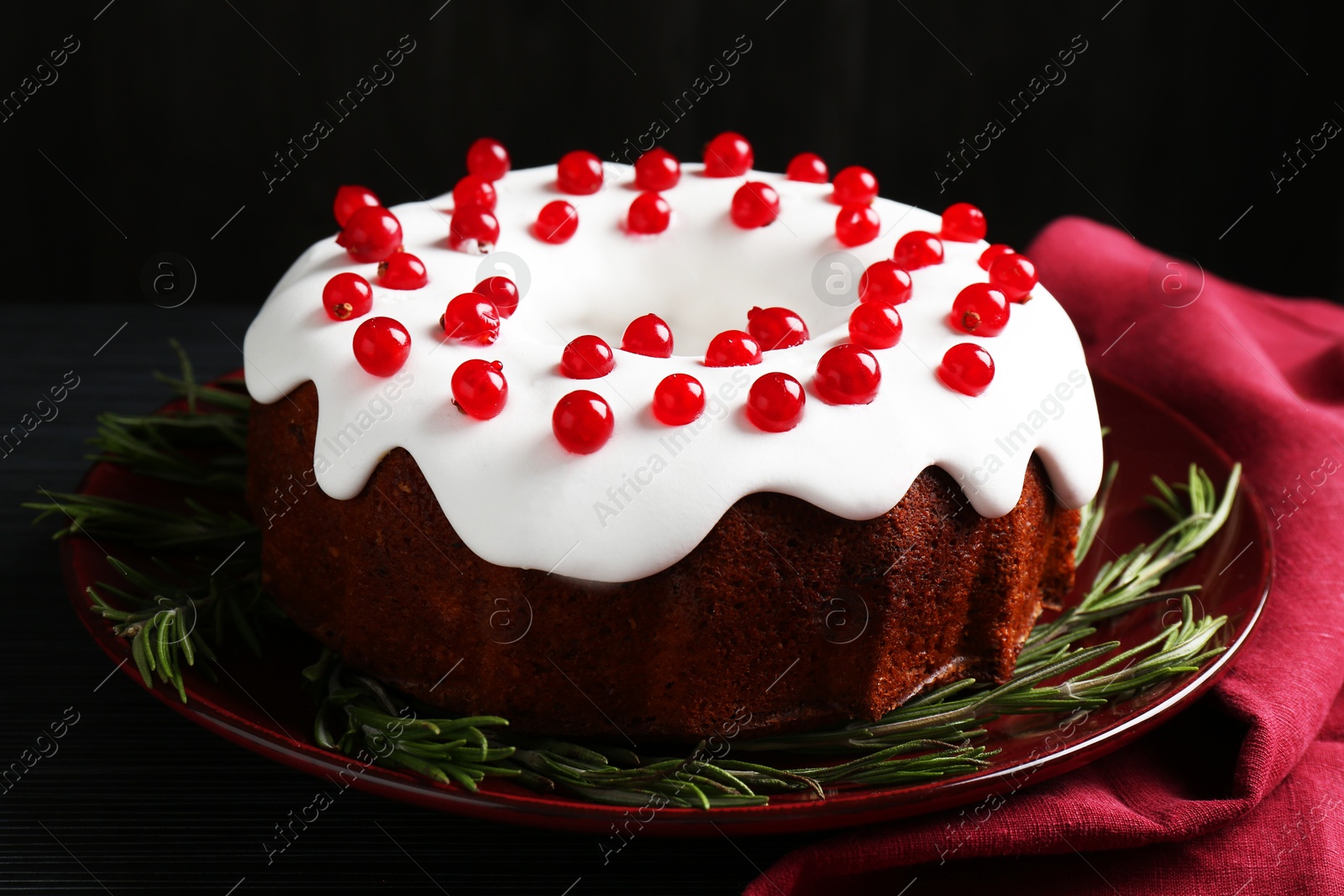 Photo of Tasty Christmas cake with red currants and rosemary on black table, closeup