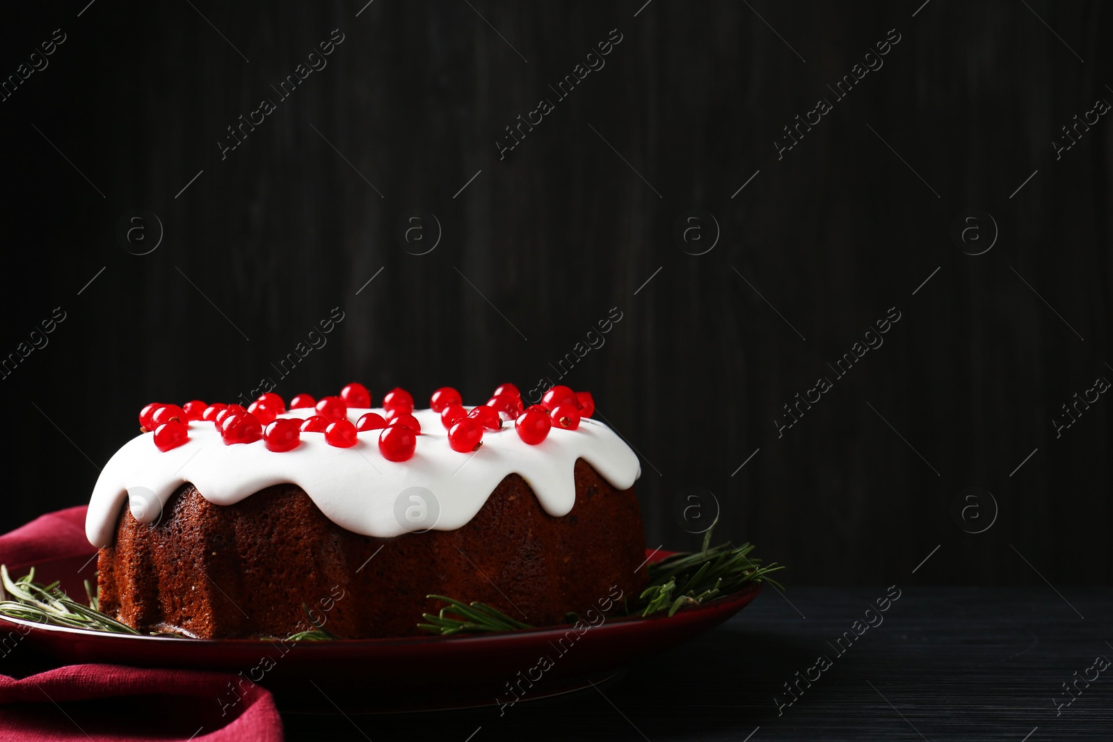 Photo of Tasty Christmas cake with red currants and rosemary on black wooden table against dark background, space for text