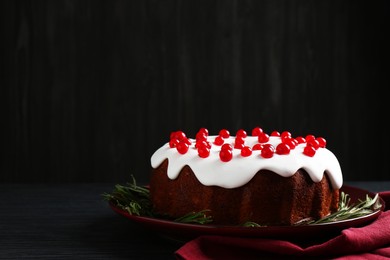 Photo of Tasty Christmas cake with red currants and rosemary on black wooden table against dark background, space for text