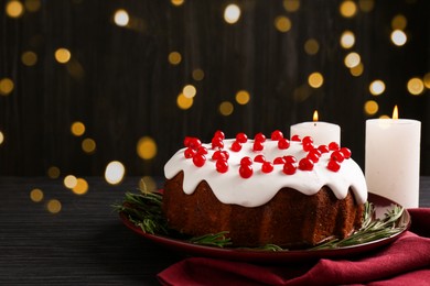 Photo of Tasty Christmas cake with red currants and rosemary on black wooden table against blurred lights, closeup