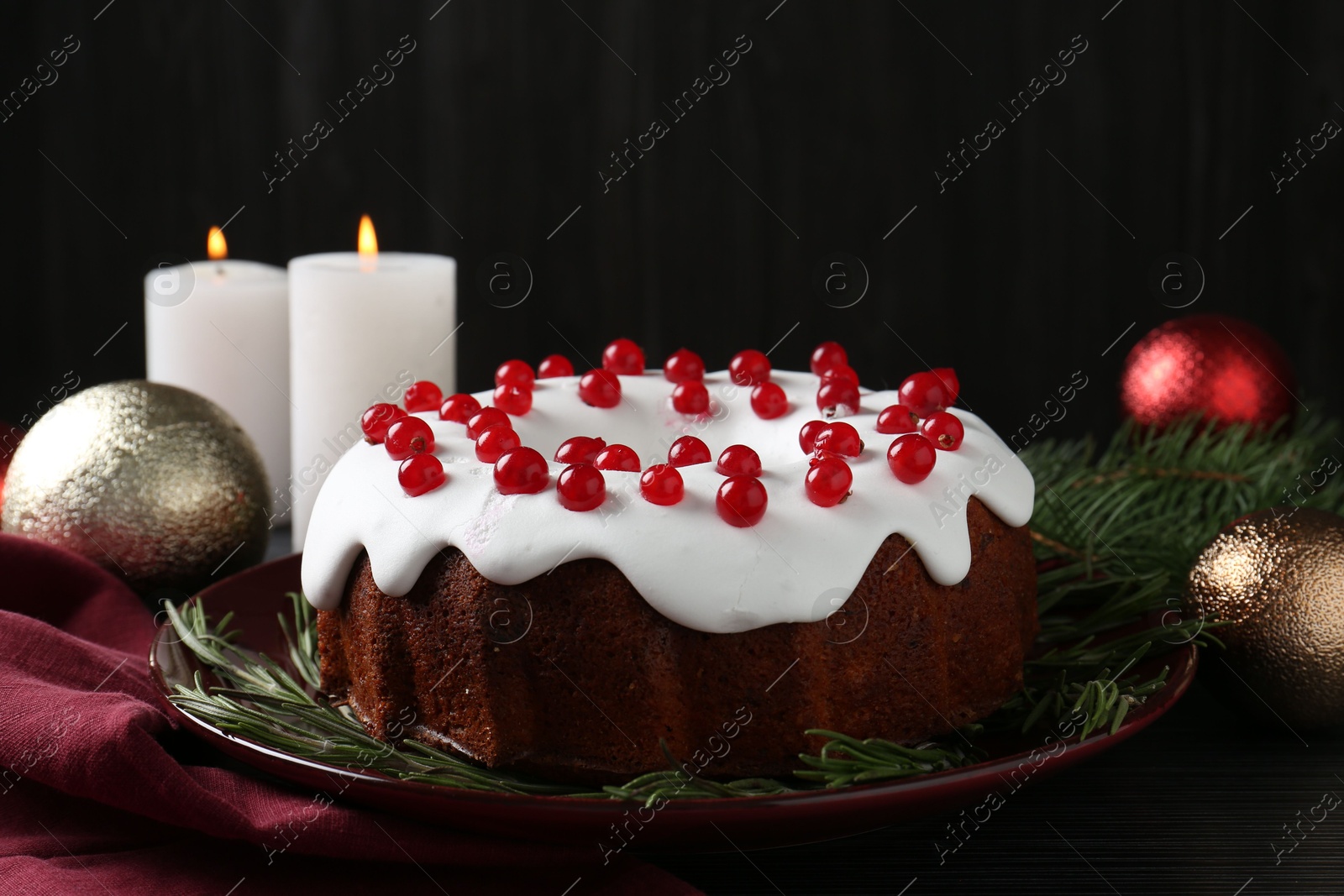 Photo of Tasty Christmas cake with red currants and rosemary on black wooden table, closeup