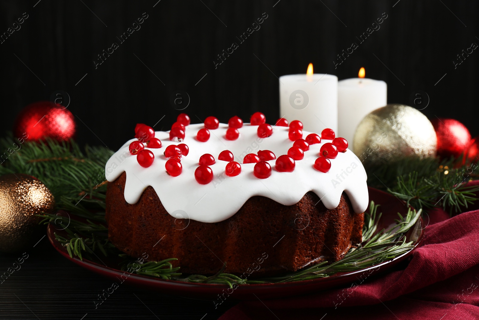 Photo of Tasty Christmas cake with red currants and rosemary on black wooden table, closeup