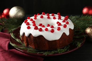 Photo of Tasty Christmas cake with red currants and rosemary on black wooden table, closeup