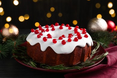 Photo of Tasty Christmas cake with red currants and rosemary on black wooden table, closeup