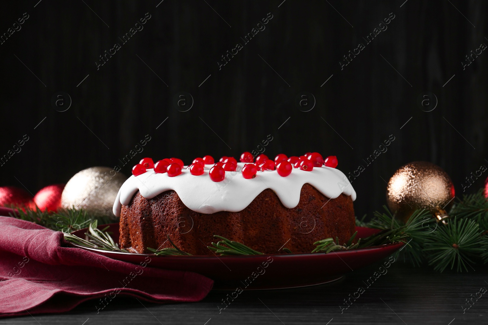 Photo of Tasty Christmas cake with red currants and rosemary on black wooden table