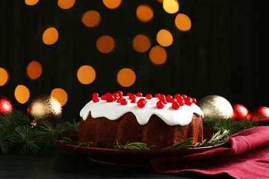 Photo of Tasty Christmas cake with red currants and rosemary on black wooden table against blurred lights, closeup