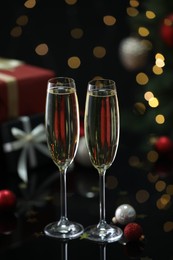 Photo of Delicious champagne in glasses and Christmas decor on black mirror surface against blurred lights, closeup