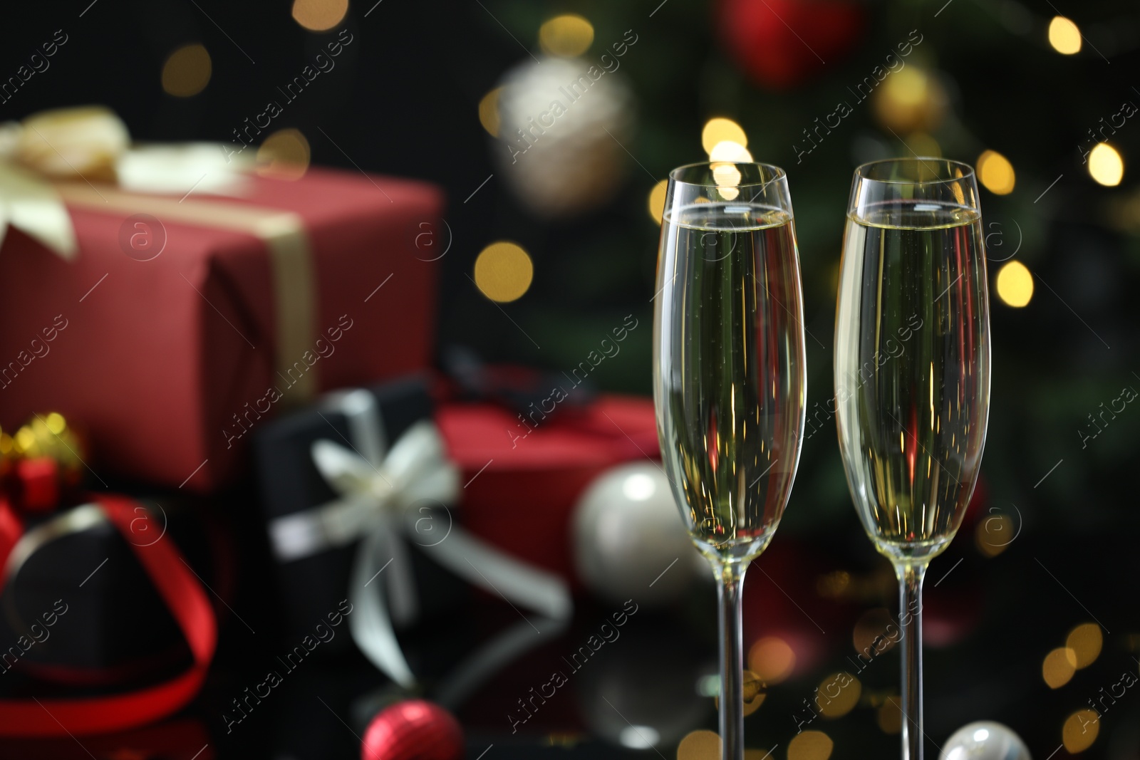 Photo of Delicious champagne in glasses and Christmas presents against blurred lights, closeup. Space for text