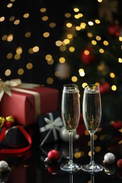 Photo of Delicious champagne in glasses and Christmas decor on black mirror surface against blurred lights. Space for text