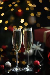 Photo of Delicious champagne in glasses and Christmas decor on black mirror surface against blurred lights, closeup